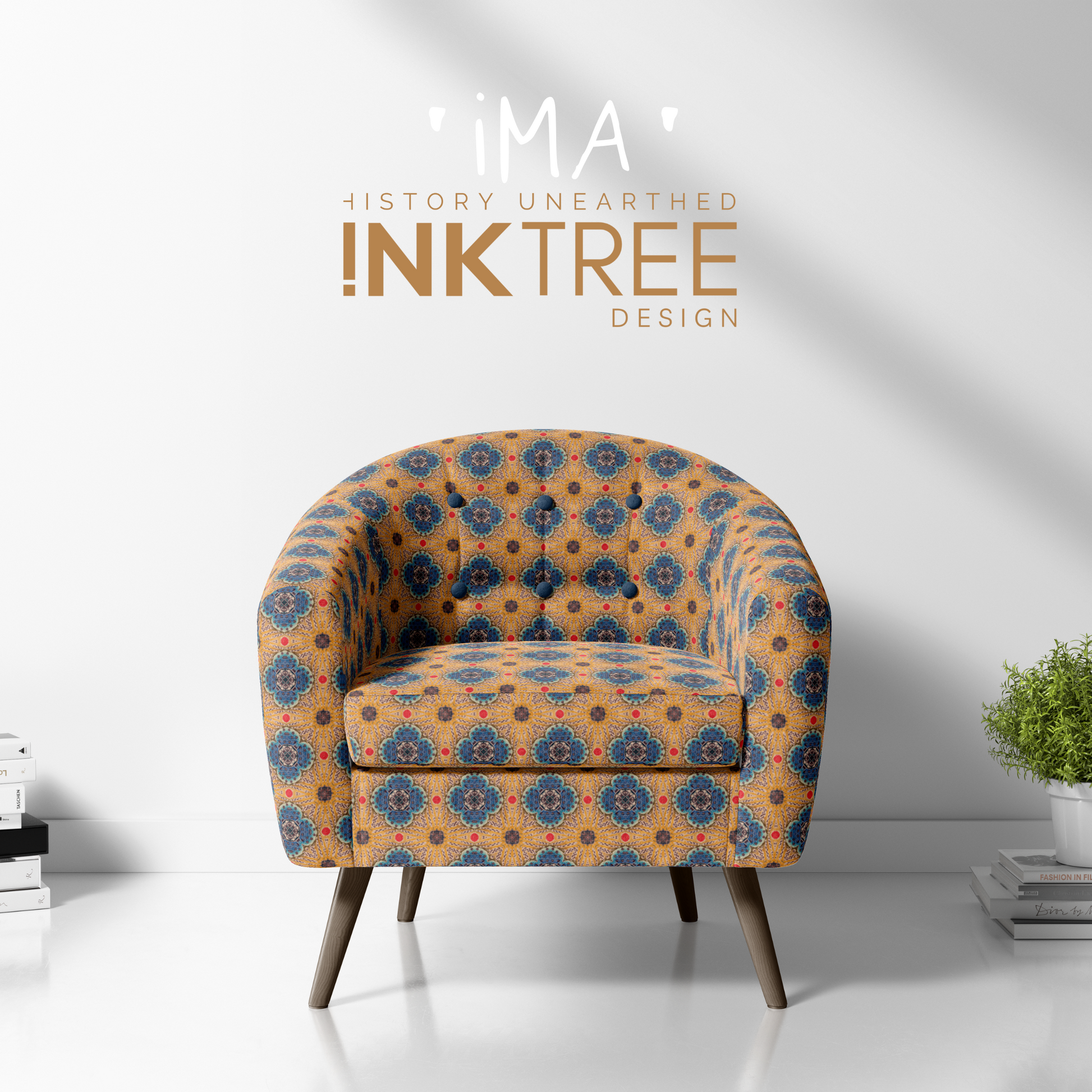 A club chair with a gold, black, blue, red and white oriental looking pattern on it with a white wall background and books and pot plant on the floor.  There is a ima history unearthered ink tree design logo on it.