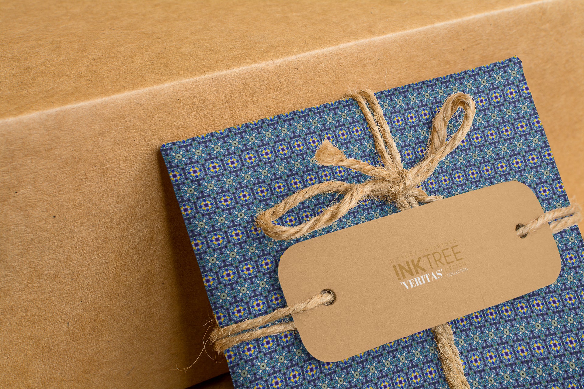 A wrapped present with brown paper in the background.  Tied with brown twine and brown tag, with blue and pink pattern.