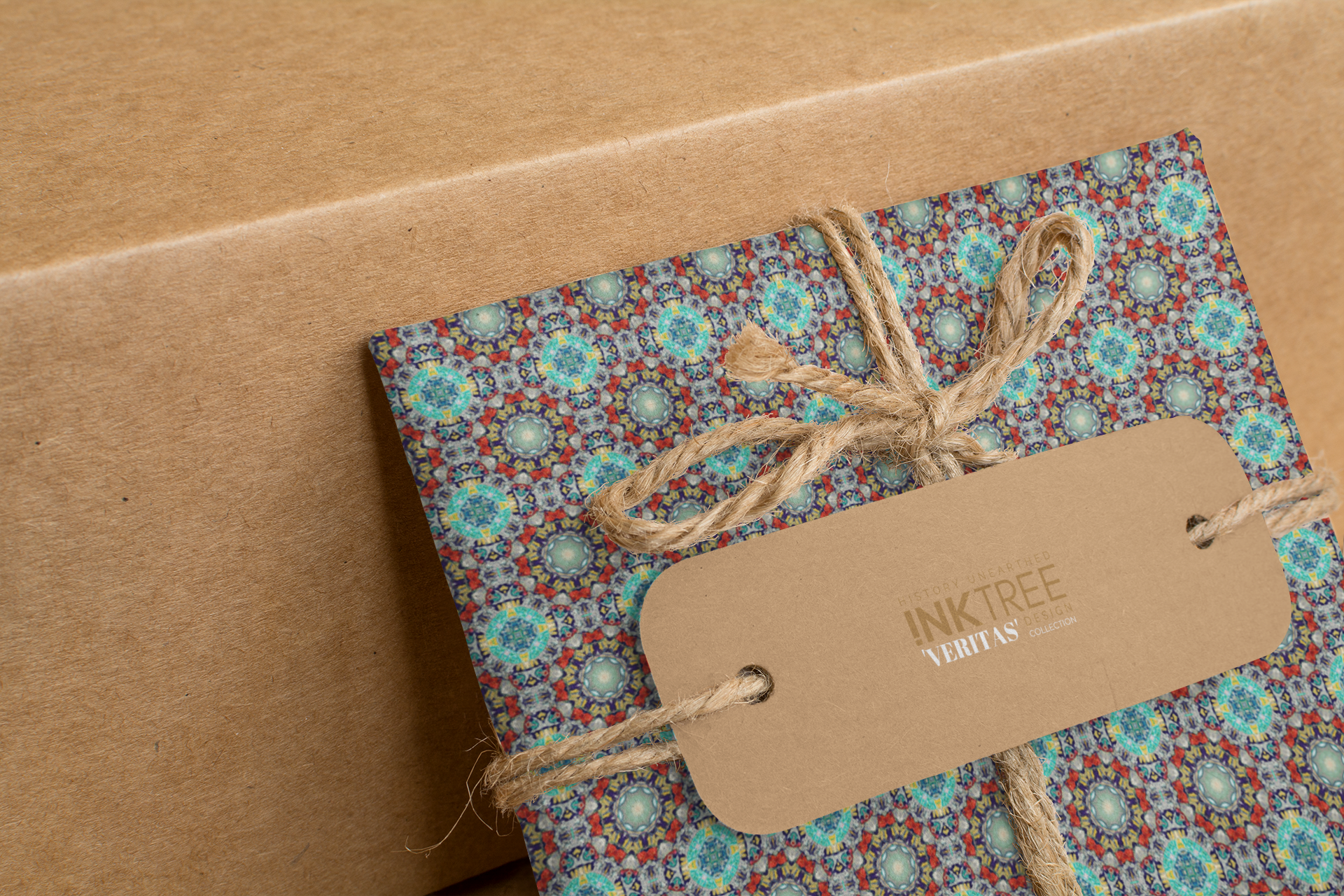 A wrapped present with brown paper in the background.  Tied with brown twine and brown tag, with blue, yellow, red and aqua pattern.