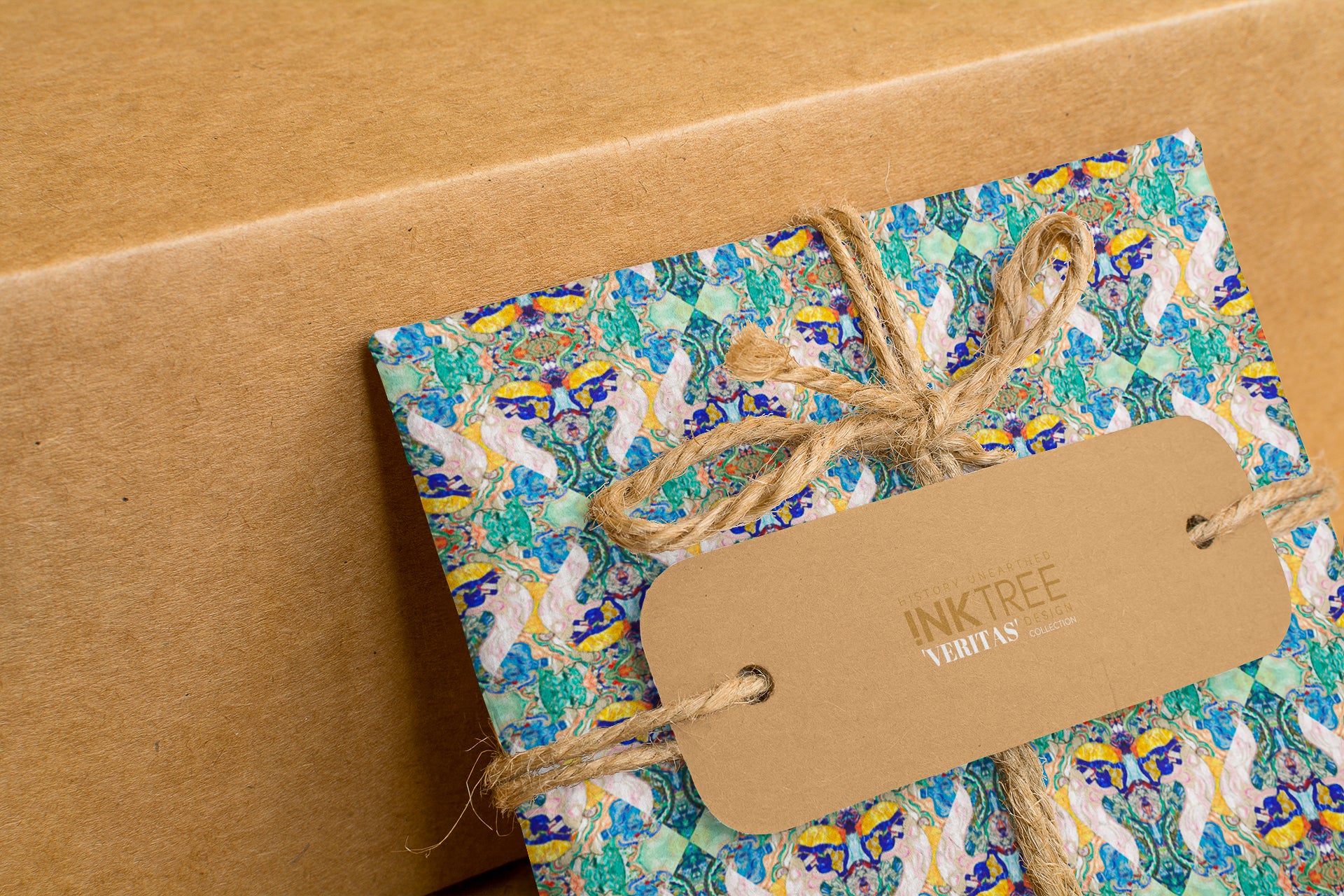 A wrapped present with brown paper in the background.  Tied with brown twine and brown tag, with blue, green and gold pattern.