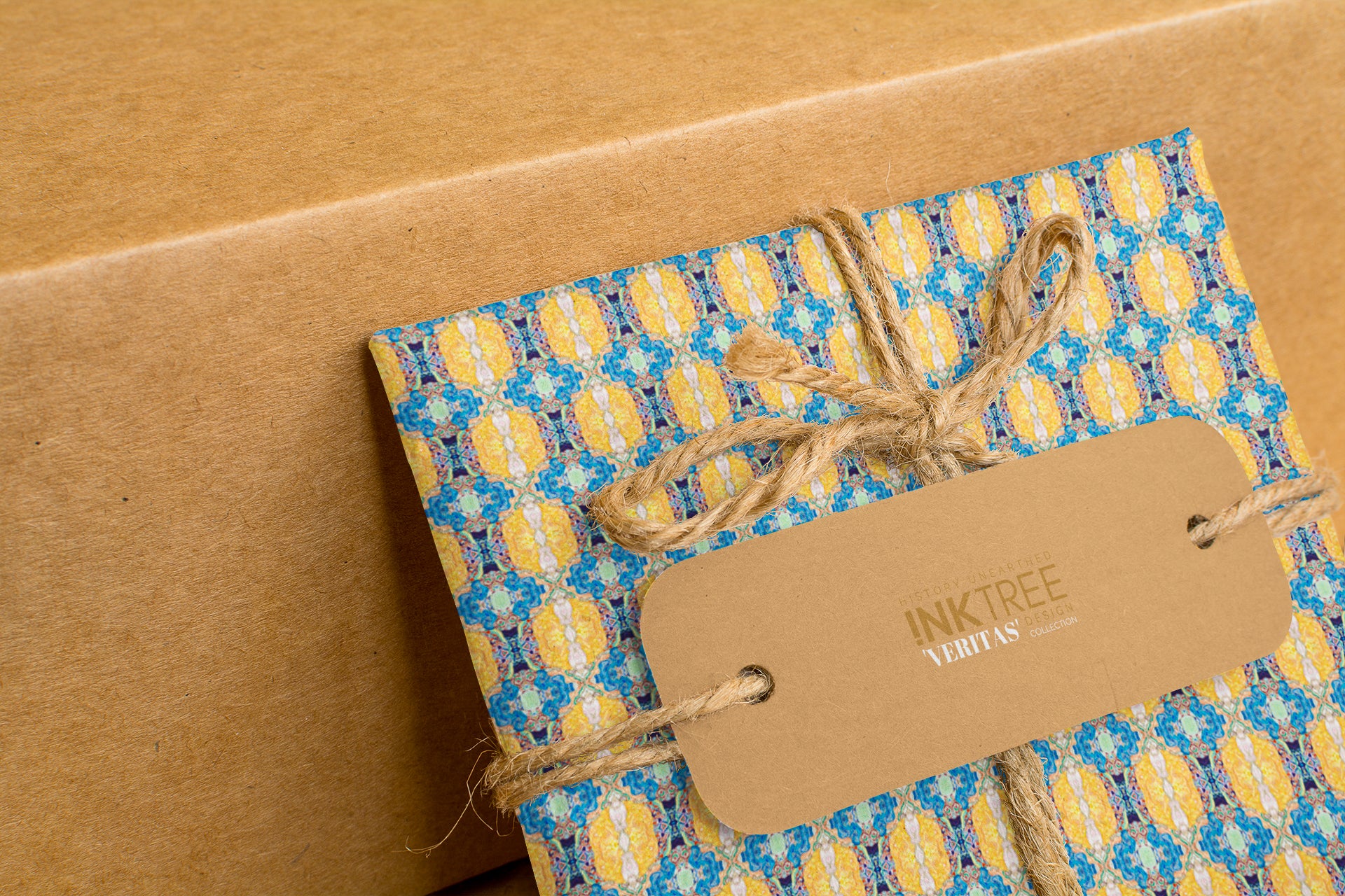 A wrapped present with brown paper in the background.  Tied with brown twine and brown tag, with blue and yellow and green pattern.