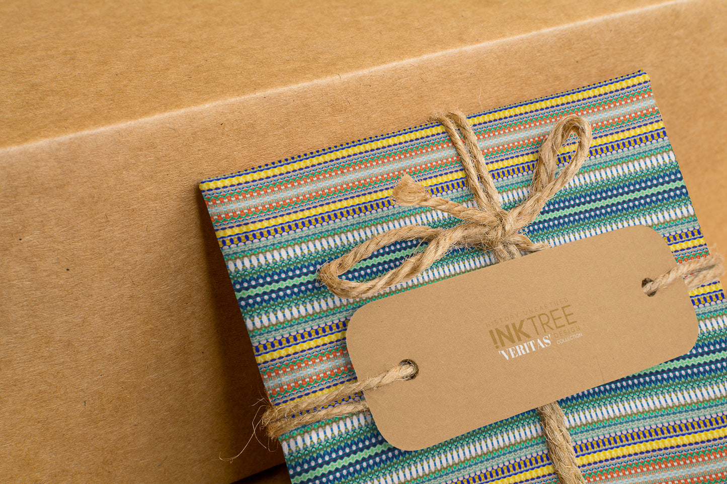 A wrapped present with brown paper in the background.  Tied with brown twine and brown tag, with blue and yellow and green pattern.