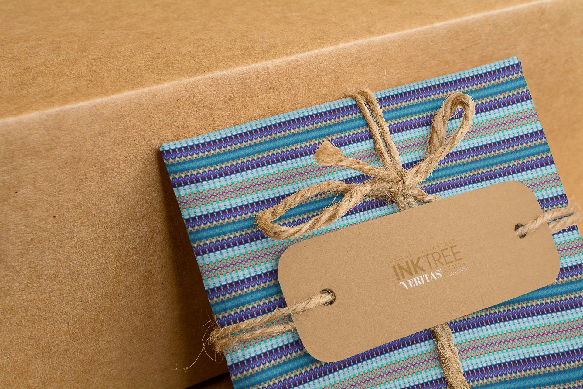 A wrapped present with brown paper in the background.  Tied with brown twine and brown tag, with blue, purple and green horizontal pattern.