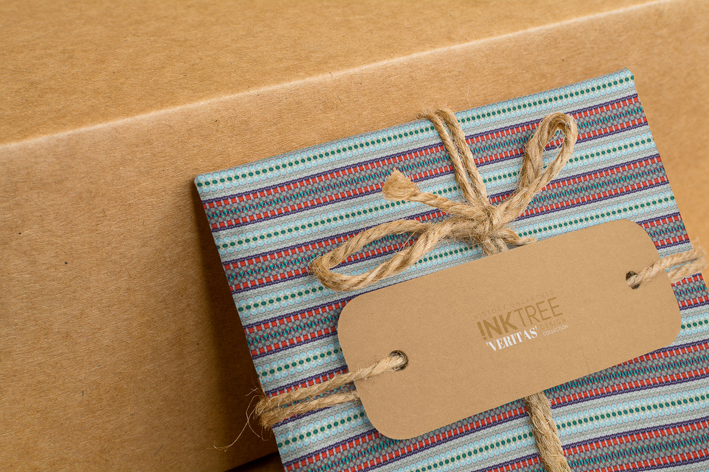 A wrapped present with brown paper in the background.  Tied with brown twine and brown tag, with blue, red and green horizontal line pattern.