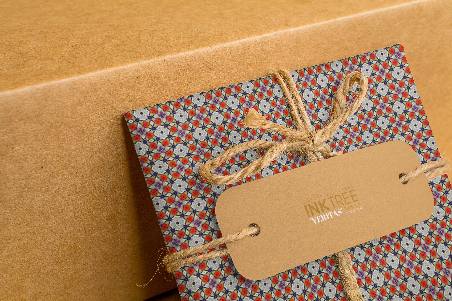 A present wrapped with blue, red and grey floral patterned paper, with a brown craft paper tag, tied with brown twine.  The background is brown craft warpping paper.